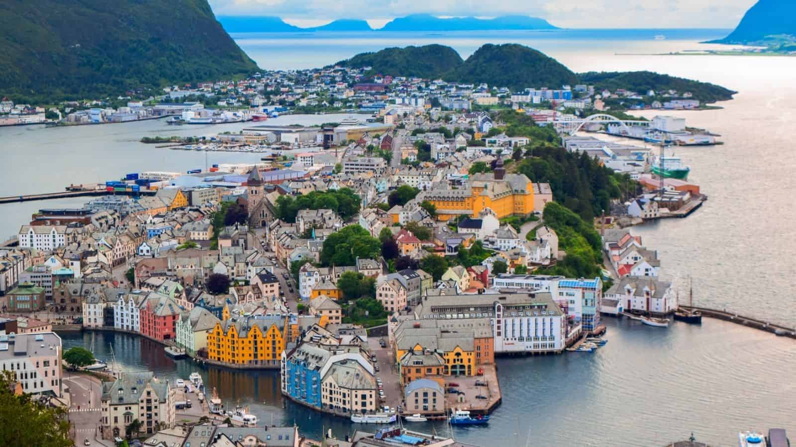 Aerial view of a coastal town with colorful buildings, surrounded by water and green hills.
