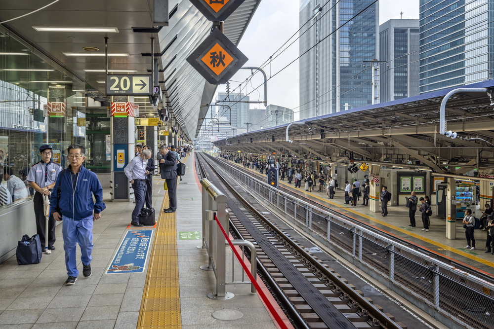 People waiting on a busy train platform in a modern city, surrounded by tracks and high-rise buildings, capture the essence of traveling in Japan.