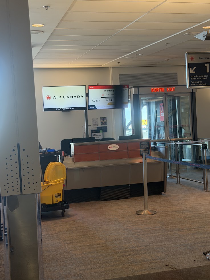 Air Canada gate at an airport with check-in counter, cleaning cart, and boarding area visible&mdash;a perfect starting point for your adventure to experience the awe-inspiring Churchill northern lights tour.