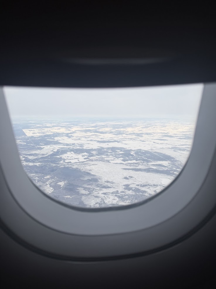 Aerial view of snowy landscape seen through an airplane window under a cloudy sky, reminiscent of the breathtaking vistas experienced on a Churchill northern lights tour.
