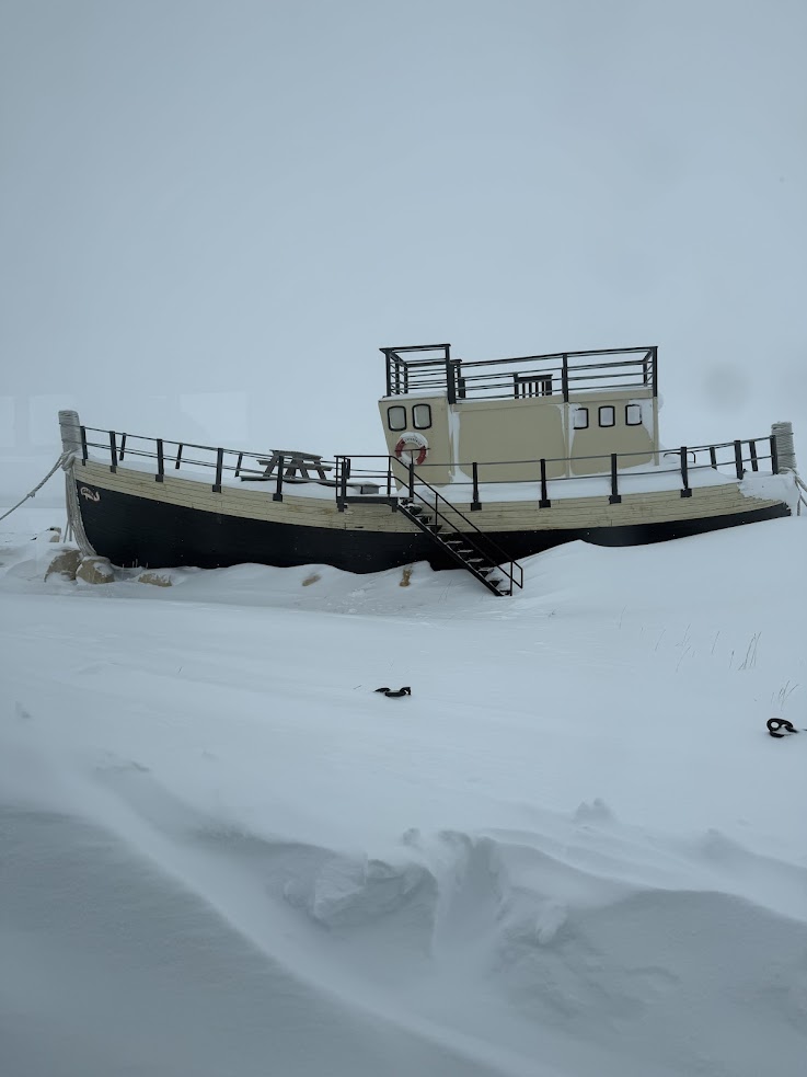 A boat sits on snowy ground in foggy weather, with a staircase leading up to its deck&mdash;reminiscent of a serene scene one might witness on a Churchill northern lights tour.