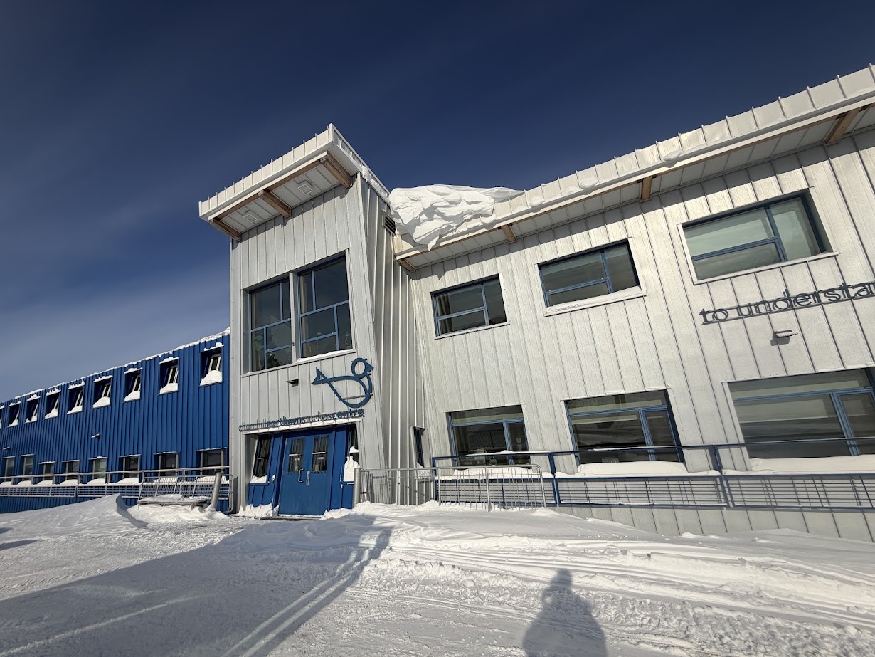 A blue and white building with snow on the roof and ground under a clear sky, reminiscent of the serene landscapes you might encounter during a Churchill Northern Lights tour.