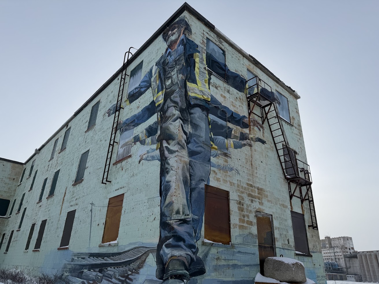 Mural of a construction worker painted on a worn building with boarded-up windows and fire escapes, reminiscent of scenes you might spot while exploring urban landscapes on a Churchill Northern Lights tour.
