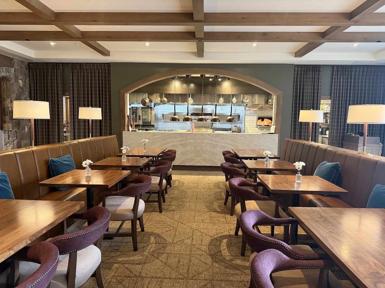 A modern restaurant with brown booths, wooden tables, purple chairs, and an open kitchen in the background, reminiscent of the inviting ambiance found at the Rusty Parrot Lodge and Spa.
