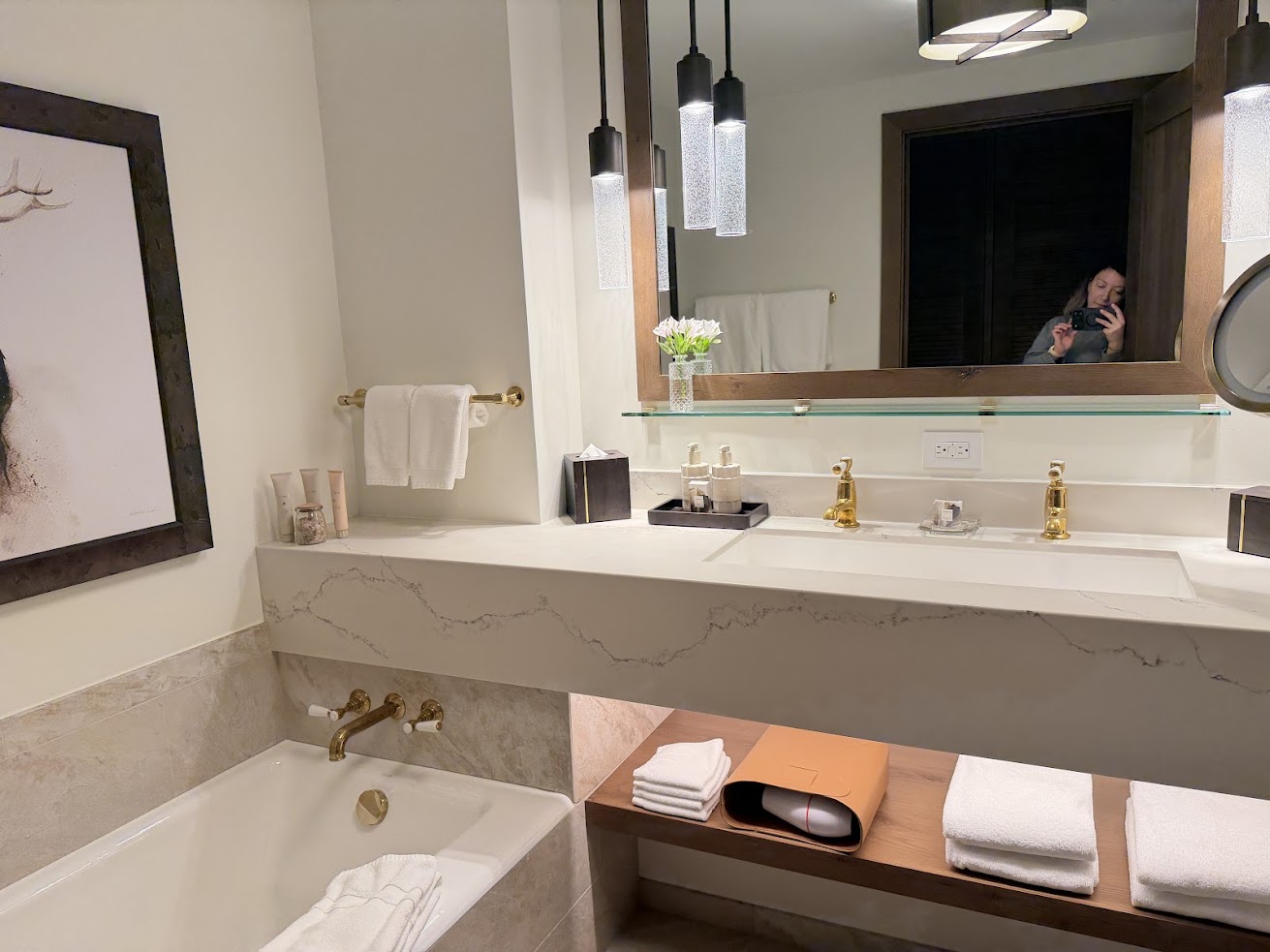 Modern bathroom at the Rusty Parrot Lodge and Spa featuring a bathtub, double sink, towels, gold fixtures, and a person’s reflection in the mirror.
