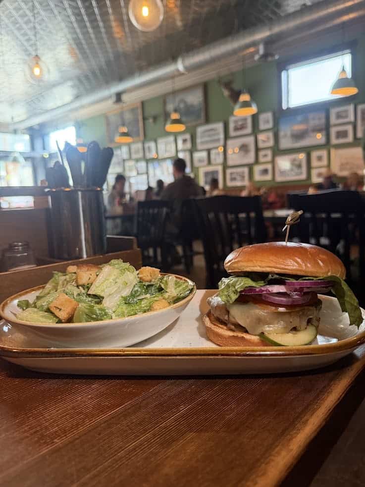 A cheeseburger with lettuce and onions, served with a Caesar salad in a cozy restaurant setting&mdash;perfect for anyone following the Jackson Hole travel guide and looking to enjoy local flavors in a warm, inviting atmosphere.