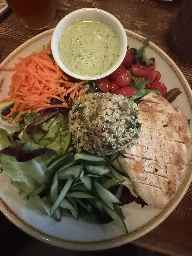 Mixed salad with quinoa, grilled chicken, carrots, cucumber, tomatoes, fresh greens, and a green dressing on the side&mdash;a refreshing meal inspired by flavors you might discover in a Jackson Hole travel guide.