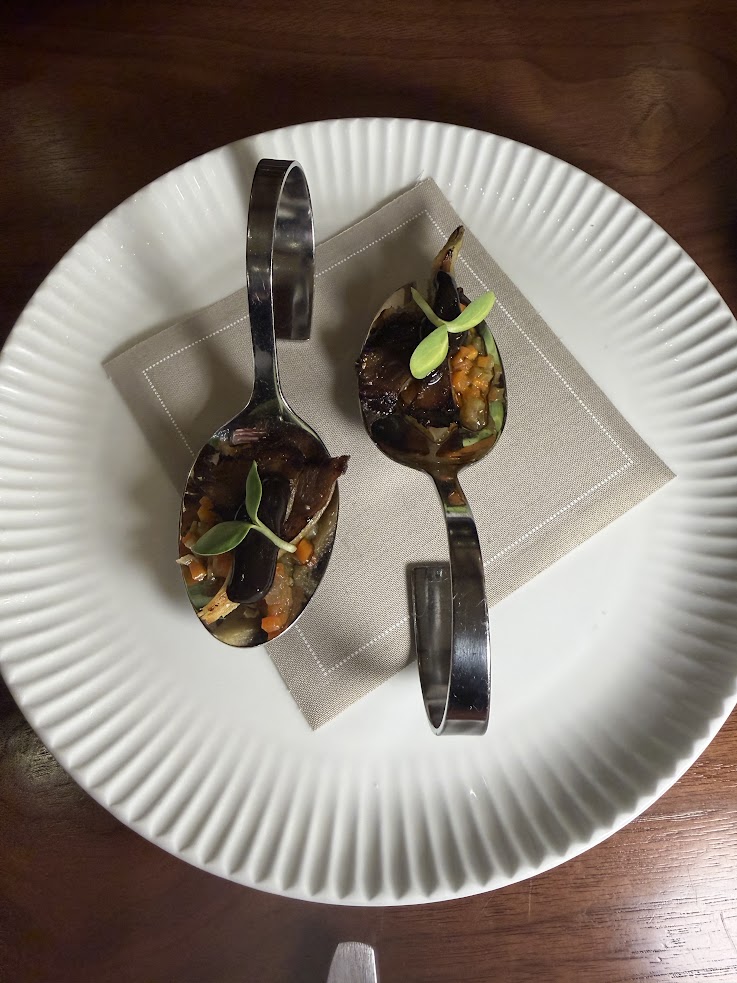 Two metal spoons with gourmet bites and microgreens on a napkin, set on a white plate—an elegant touch inspired by the refined dining experiences at Rusty Parrot Lodge and Spa.