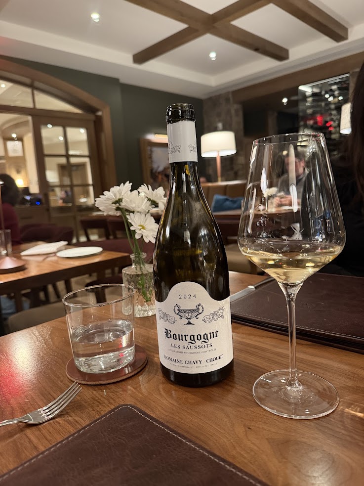 A bottle of white wine, a filled glass, water, and flowers are beautifully arranged on a wooden restaurant table at the Rusty Parrot Lodge and Spa.