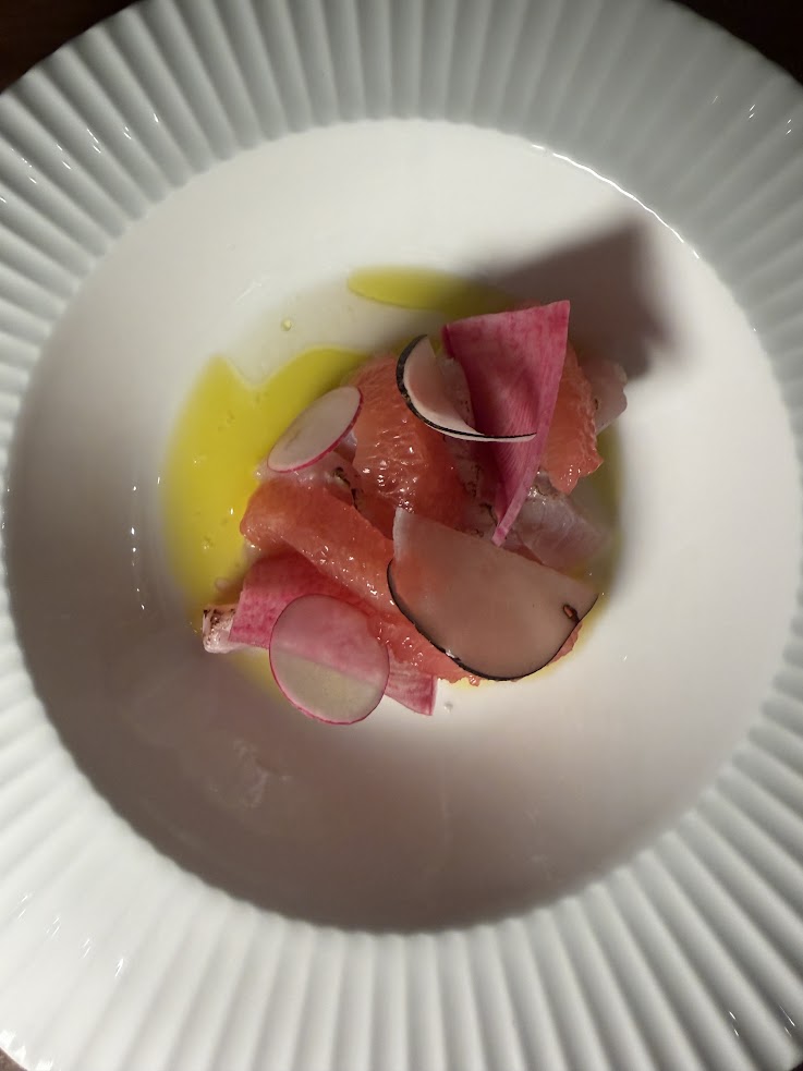 Thin grapefruit slices, radishes, and dressing arranged on a white, ridged plate evoke the elegant presentation found at Rusty Parrot Lodge and Spa.