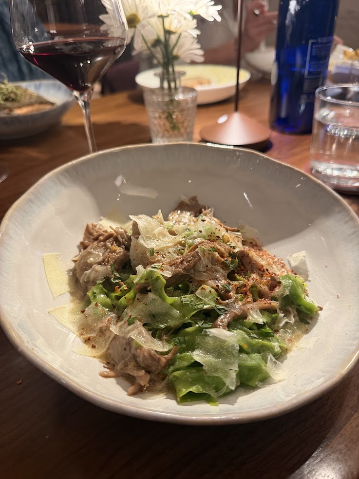 Bowl of shredded meat with lettuce, cheese, and seasoning, beside a glass of red wine and a flower vase—an inviting scene reminiscent of the rustic elegance at the Rusty Parrot Lodge and Spa.