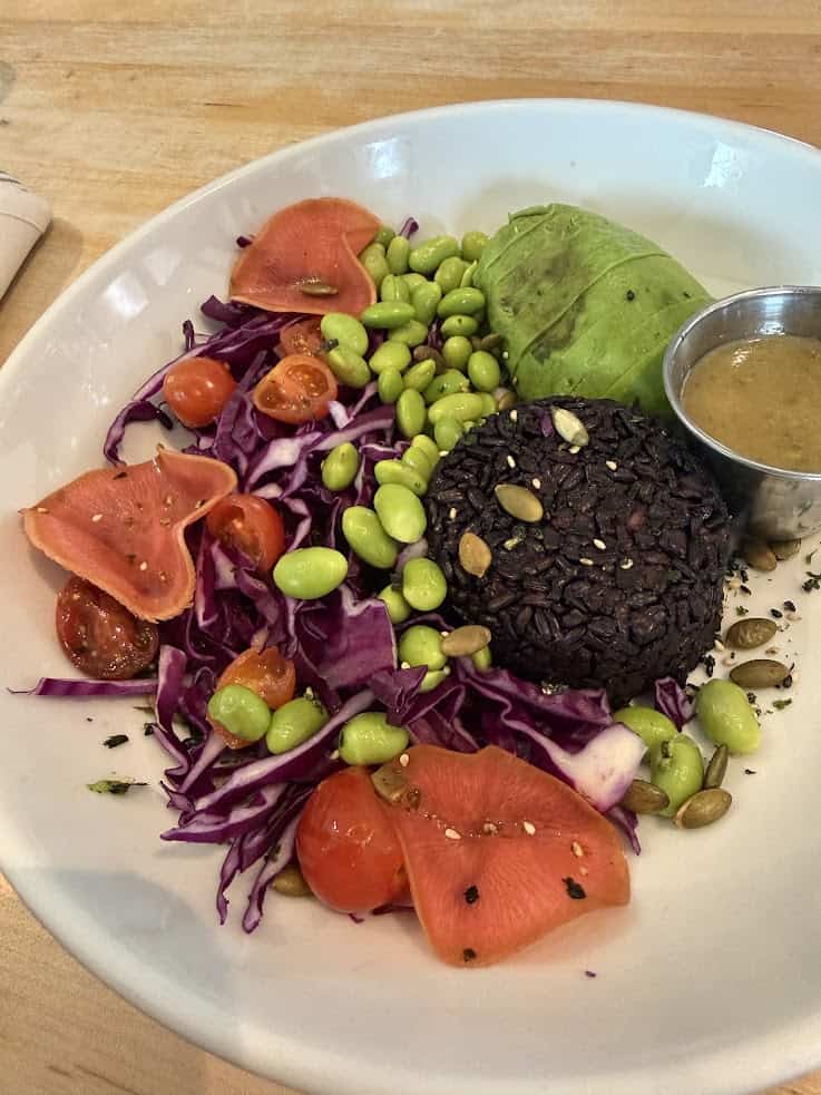 A bowl with black rice, avocado, edamame, pickled radish, grape tomatoes, red cabbage, and dressing&mdash;this vibrant dish is the kind of wholesome meal you might discover while exploring hidden gems in a Jackson Hole travel guide.