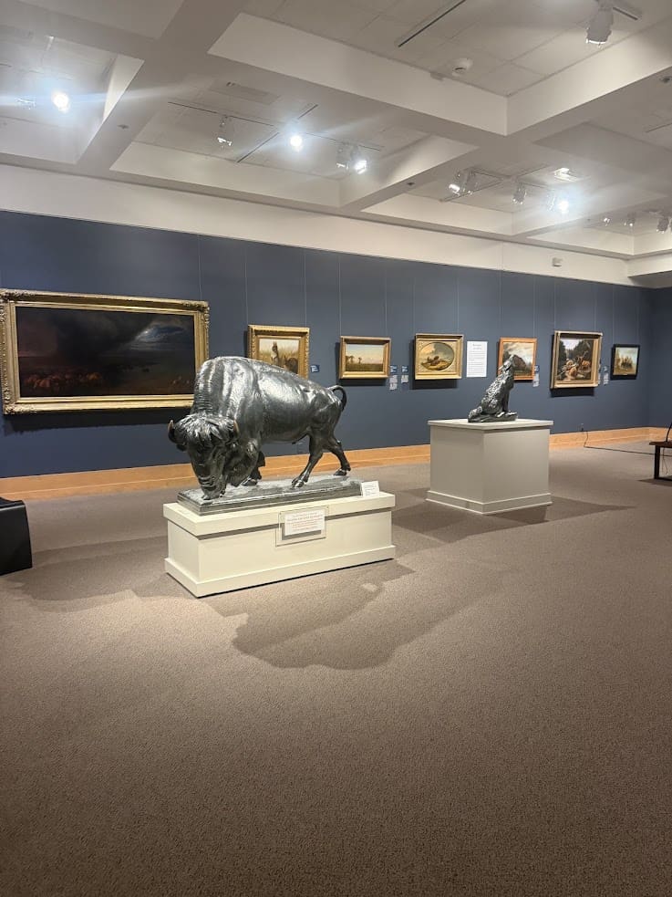 Art gallery with animal sculptures and framed paintings displayed on blue walls under bright lighting, making it a must-see stop in any Jackson Hole travel guide.