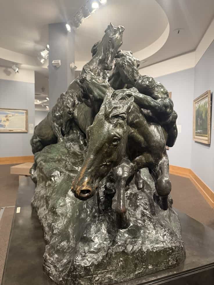 Bronze sculpture of three horses and riders leaping forward, displayed in an art museum gallery&mdash;a striking highlight often featured in a Jackson Hole travel guide.