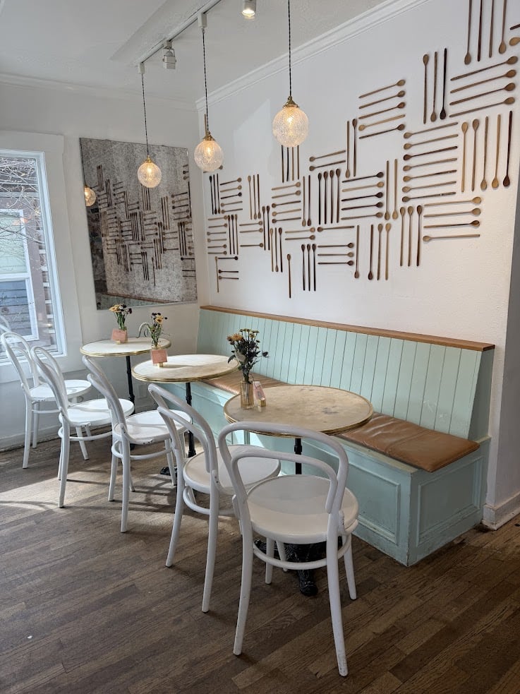Cozy caf&eacute; with white chairs, round tables, a mint bench, and wall art made of arranged wooden spoons and forks&mdash;a hidden gem often recommended in any Jackson Hole travel guide.