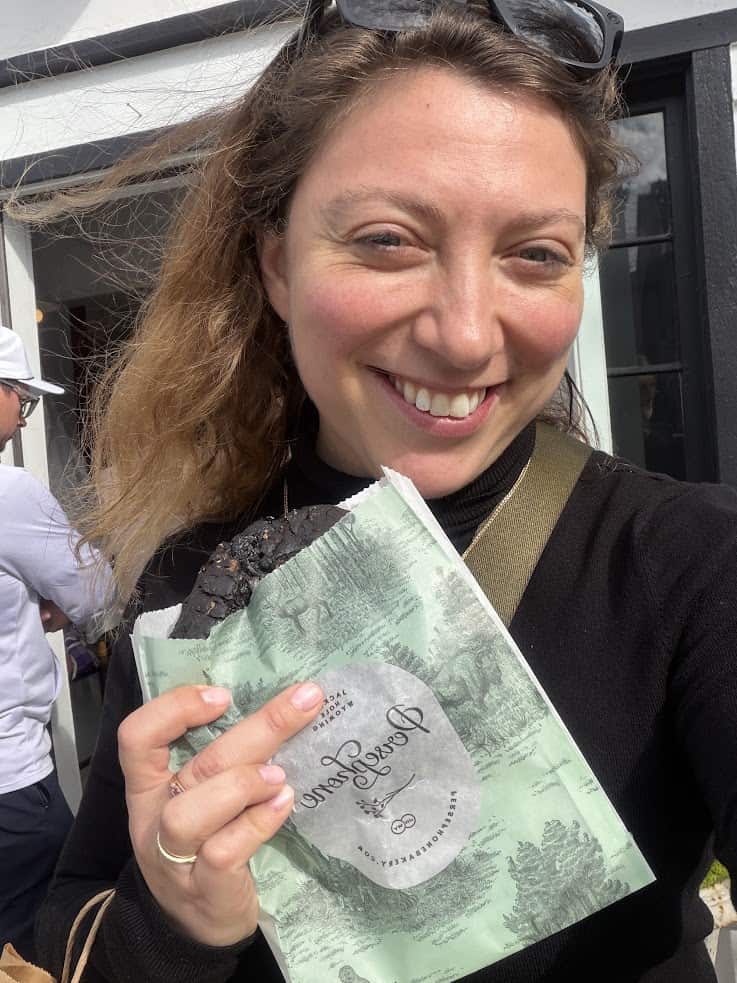 Woman smiling and holding a pastry in a green bag with script outside a building on a sunny day&mdash;just the kind of moment you&rsquo;d find in an insider&rsquo;s Jackson Hole travel guide.
