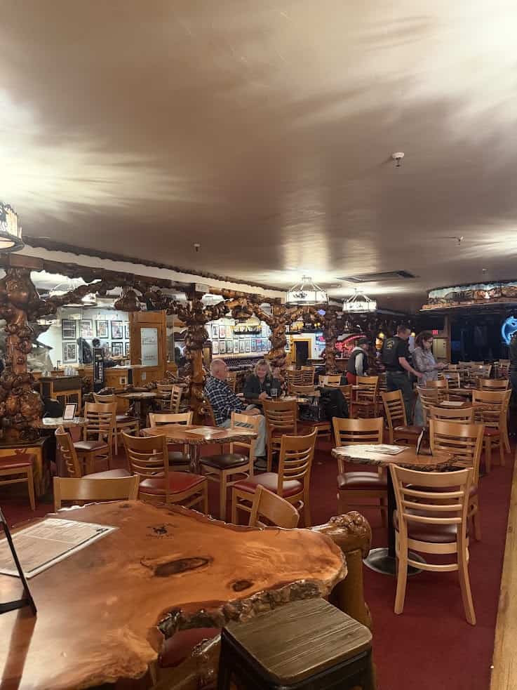Wood-themed restaurant with wooden tables and chairs, customers dining, and warm lighting throughout&mdash;a cozy spot often highlighted in the Jackson Hole travel guide for its inviting atmosphere.