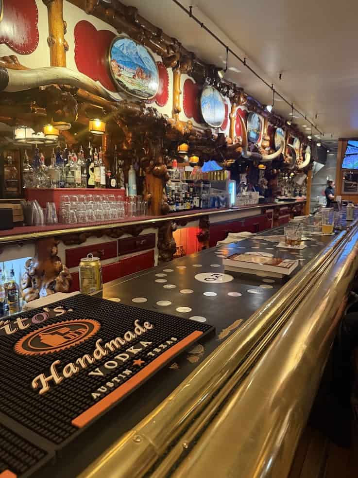 Long wooden bar with drinks, barstools, and a decorated mirror wall in a warmly lit, cozy setting&mdash;an inviting spot often featured in any comprehensive Jackson Hole travel guide.