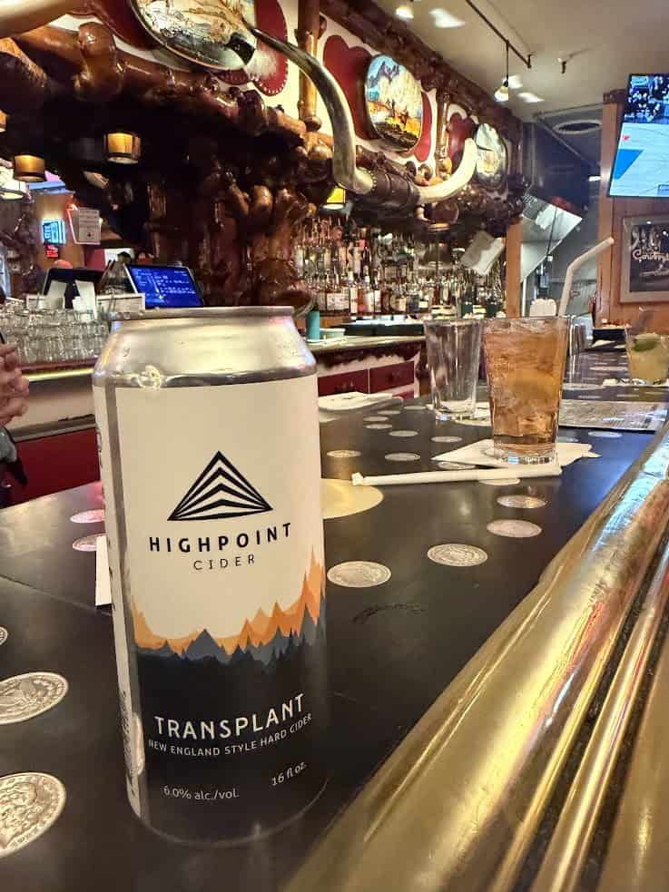 A can of Highpoint Cider on a bar counter, with drinks, decor, and TVs in the background&mdash;an inviting scene straight out of a jackson hole travel guide.