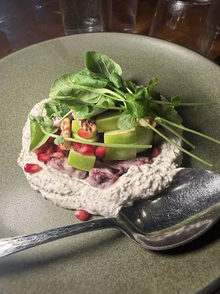 A salad with greens, apple slices, nuts, and pomegranate on creamy dressing, served on a green plate&mdash;an inviting dish reminiscent of the fresh, vibrant flavors discovered in a Jackson Hole travel guide.