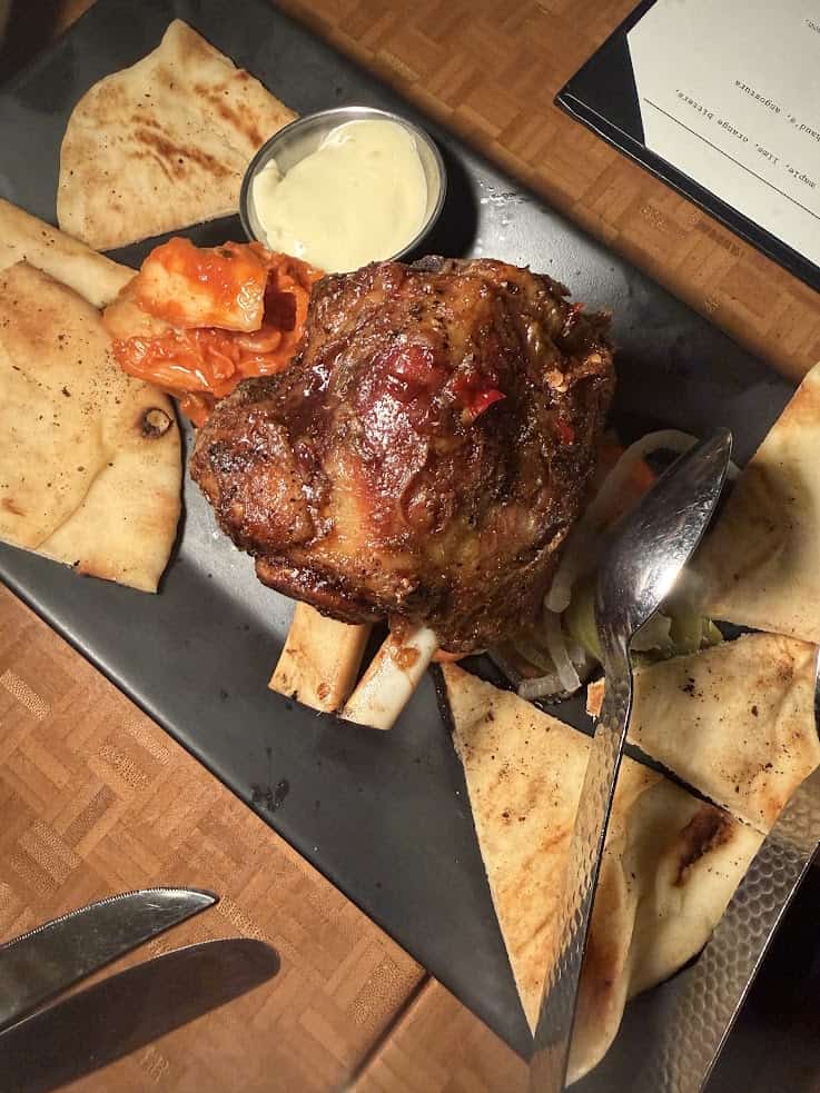 Roast meat with pita slices, kimchi, sauce, and utensils on a black plate atop a wooden table&mdash;perfect fuel while planning your next adventure with a Jackson Hole travel guide.