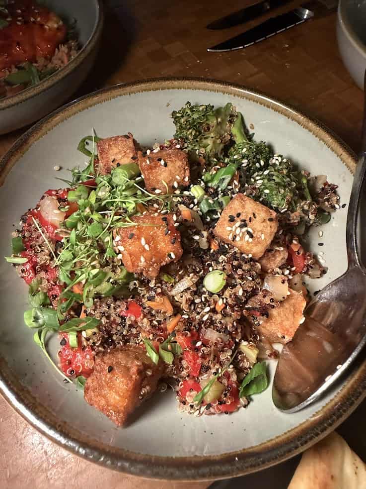 Bowl of quinoa salad with crispy tofu, vegetables, microgreens, and sesame seeds, served with a spoon beside it&mdash;a nourishing dish that would fit perfectly in any jackson hole travel guide for healthy eats.