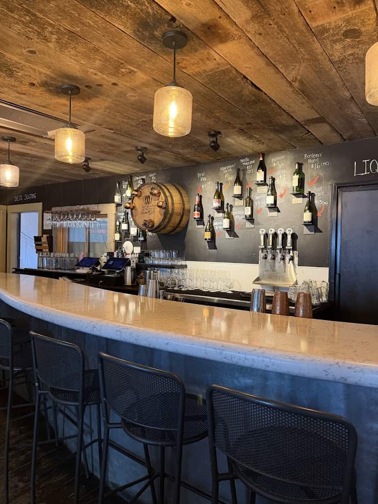 Empty bar with hanging lights, marble counter, wine bottles on the wall, and beer taps below a barrel&mdash;this inviting setting could be the perfect hidden gem in your next Jackson Hole travel guide.