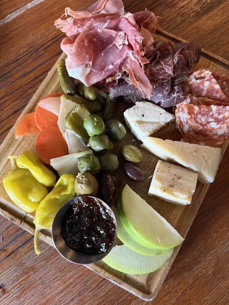 Charcuterie board with cured meats, cheeses, pickles, olives, apple slices, peppers, and a jam&mdash;perfect for savoring after a day exploring with your Jackson Hole travel guide.