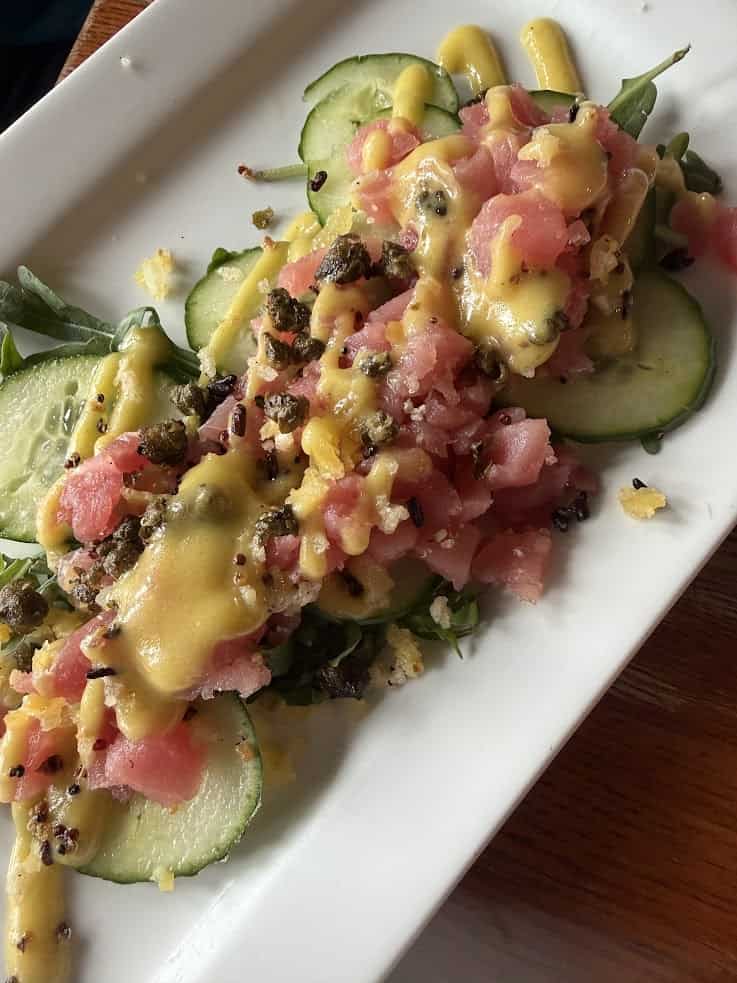Diced raw fish on sliced cucumber with greens and yellow sauce, served on a white rectangular plate&mdash;a refreshing dish that could easily grace the pages of a Jackson Hole travel guide.