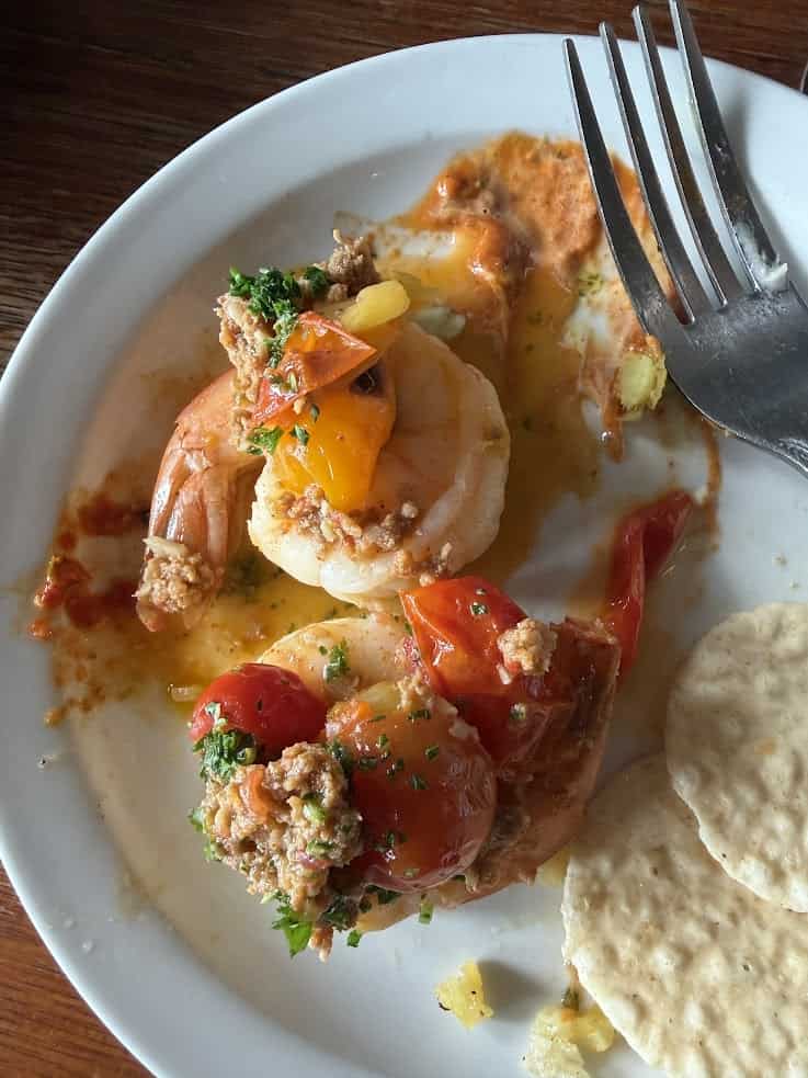 Cooked shrimp with tomatoes, herbs, and sauce on a plate, next to tortilla chips, with a fork nearby&mdash;a vibrant dish reminiscent of flavors you might discover in a Jackson Hole travel guide.