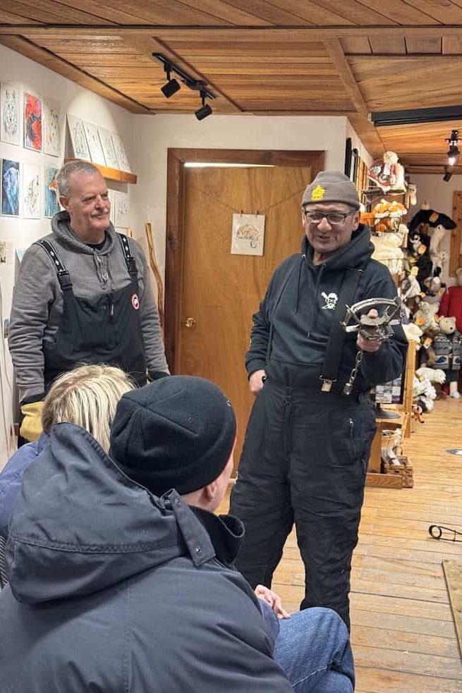 A man in winter gear holds a small animal for a seated audience in a cozy wooden room with art on the walls, offering an intimate wildlife encounter often enjoyed during a Churchill northern lights tour.