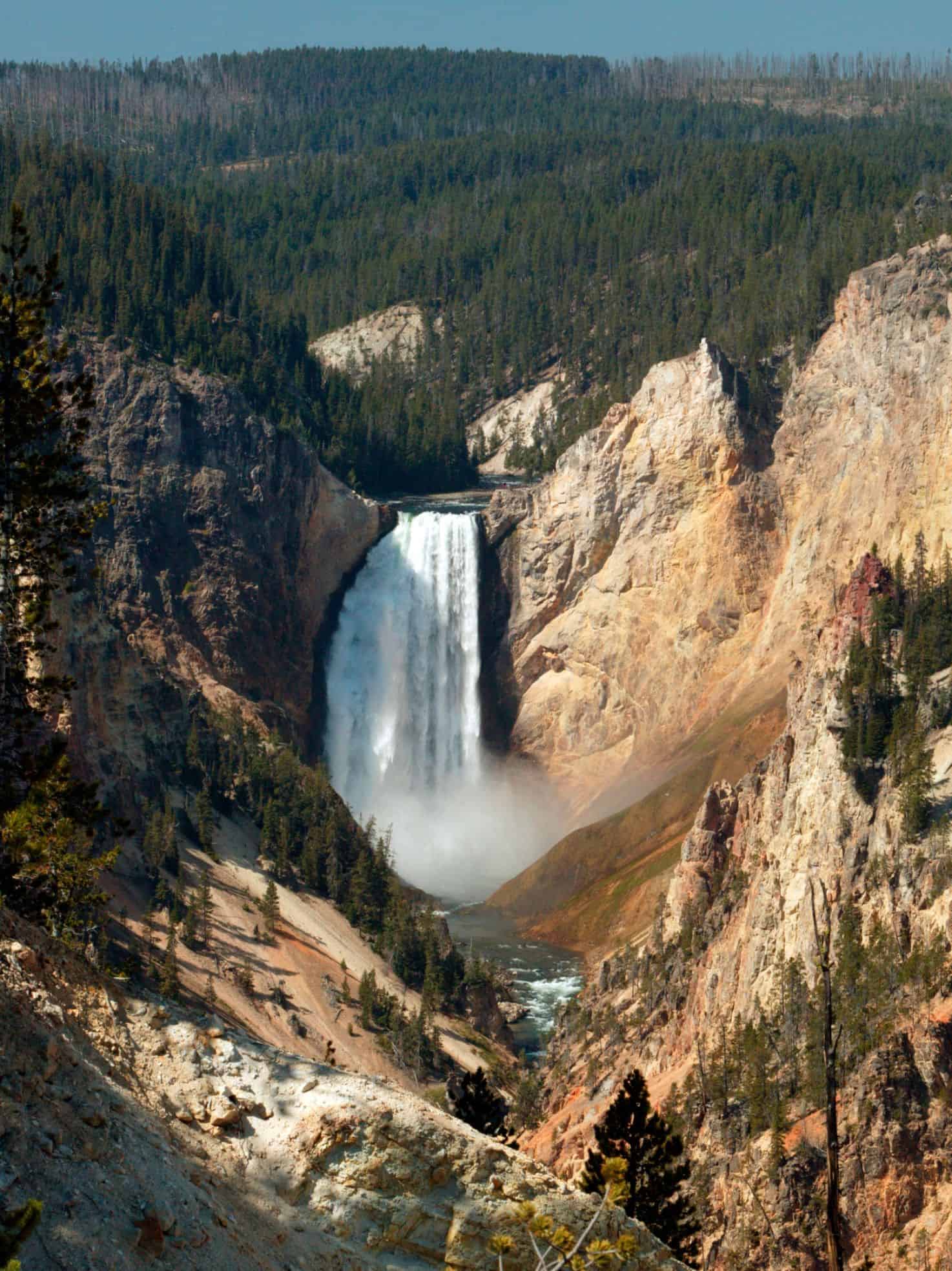 Waterfall cascading into a canyon surrounded by pine trees and rocky cliffs under a clear sky&mdash;a breathtaking scene straight out of a Jackson Hole travel guide.