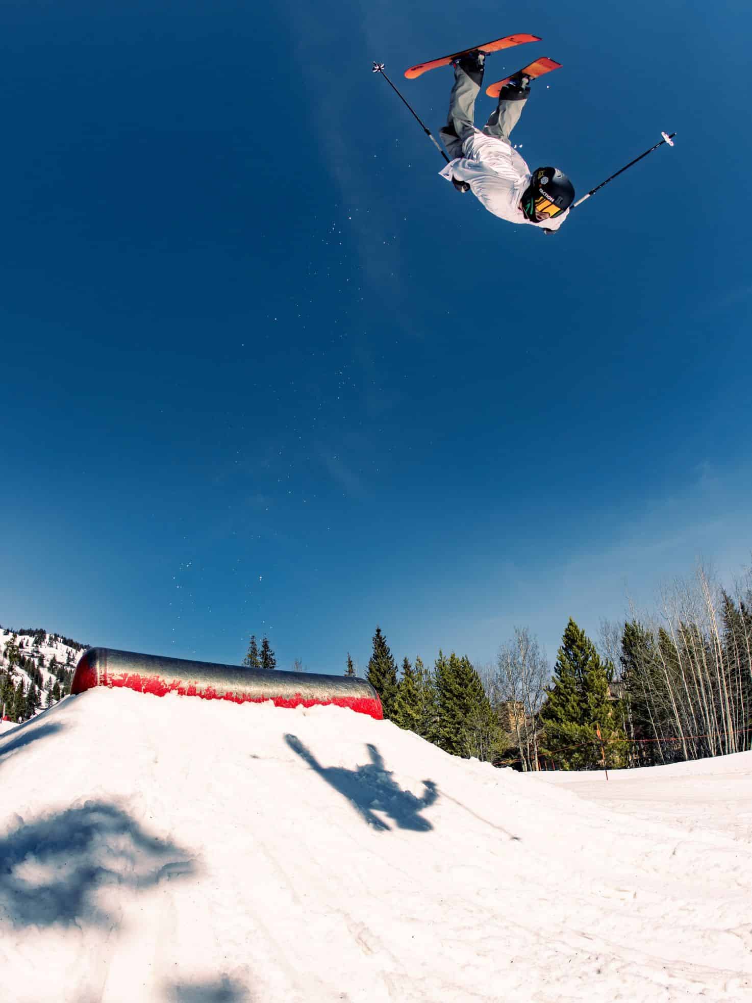 A skier performs an aerial trick above a snowy slope with trees and a clear blue sky in the background&mdash;a scene straight out of a Jackson Hole travel guide.
