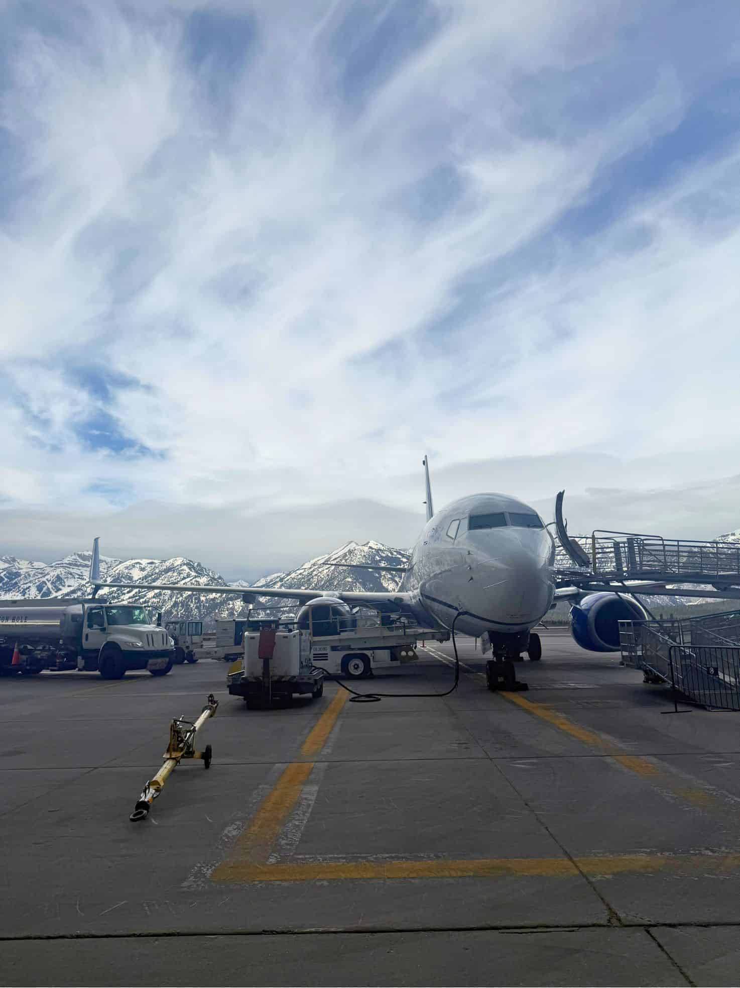 Airplane parked at an airport gate with snowy mountains and a cloudy sky in the background, offering a scene straight out of a Jackson Hole travel guide.
