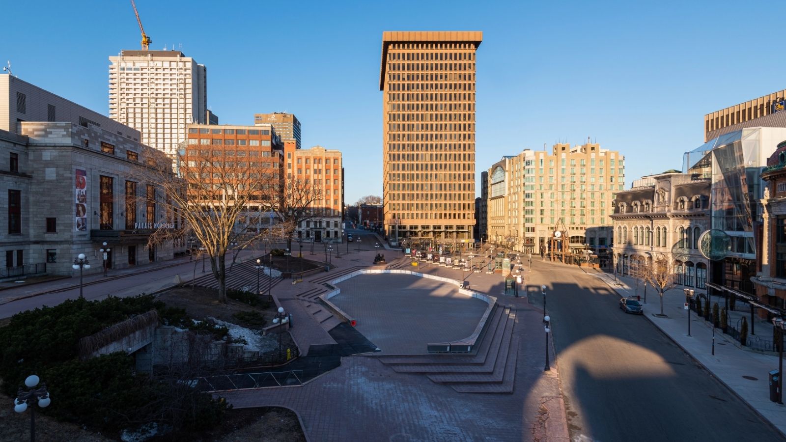 A city square with empty streets, tall buildings, and clear blue sky in the background.