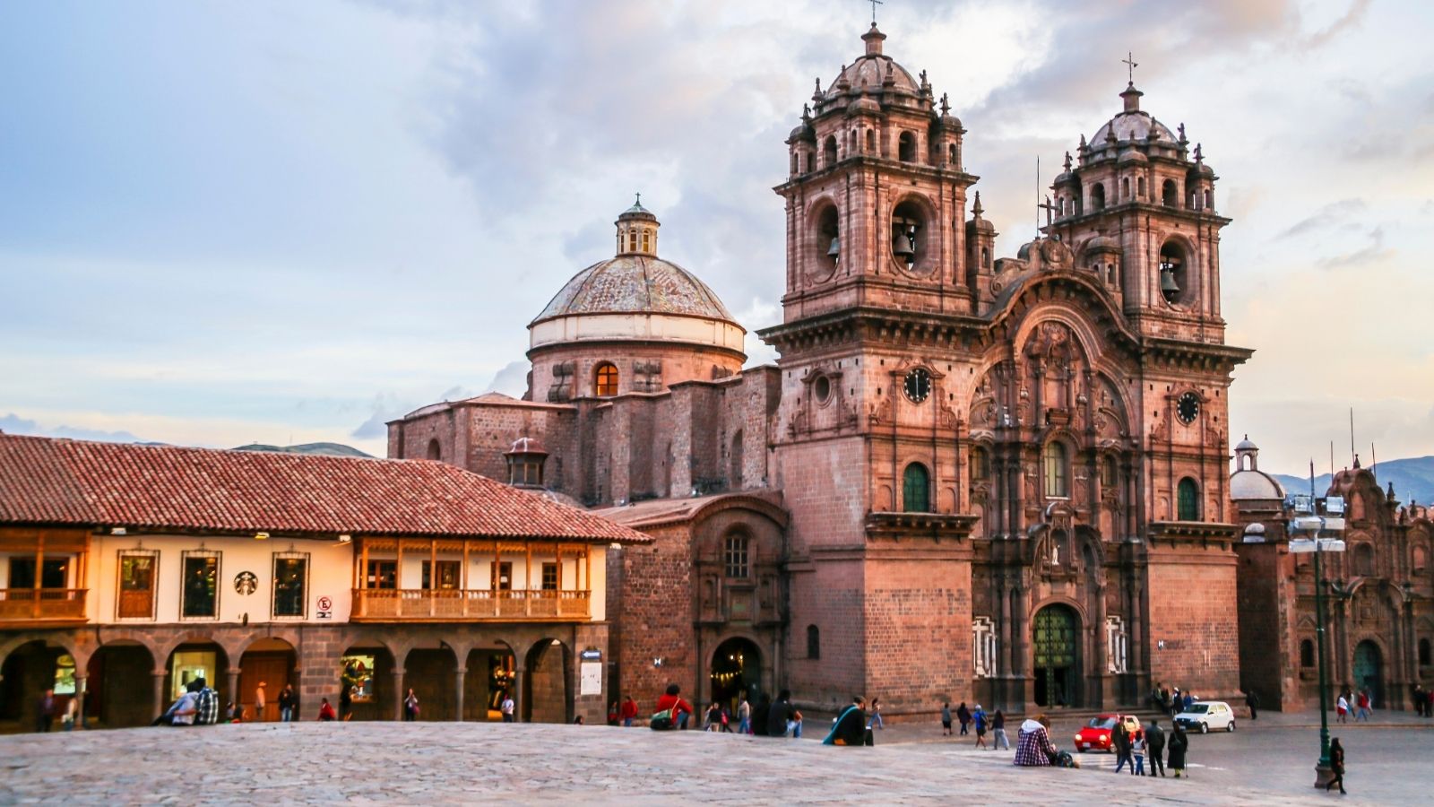 Colonial church and plaza with people walking in Cusco, Peru, at sunset.