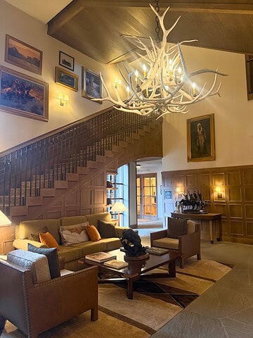 Cozy lodge lobby at the Rusty Parrot Lodge and Spa with an antler chandelier, wood accents, art on the walls, and comfy seating near a staircase.