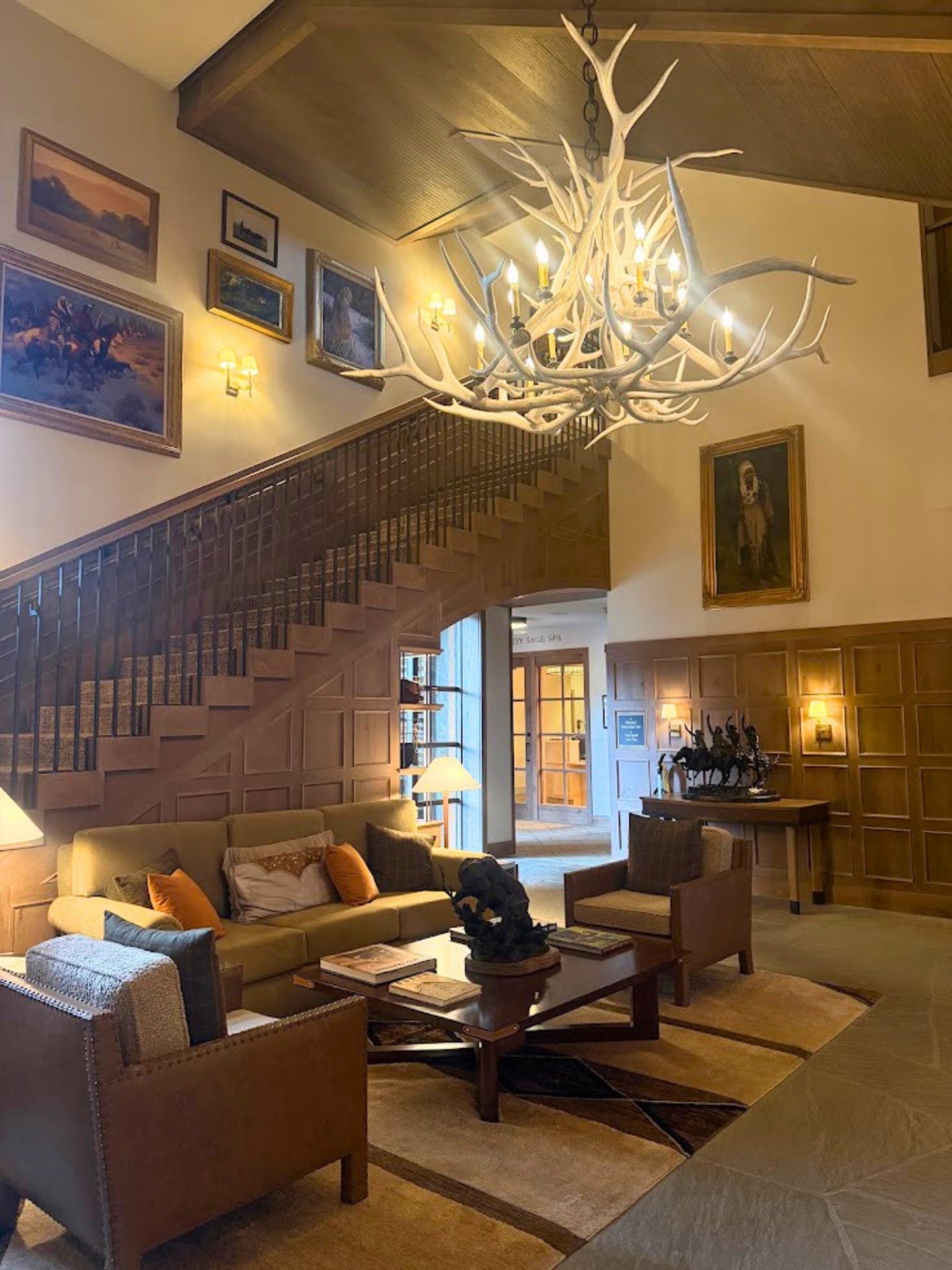 Cozy lodge lobby at the Rusty Parrot Lodge and Spa with an antler chandelier, wood accents, art on the walls, and comfy seating near a staircase.