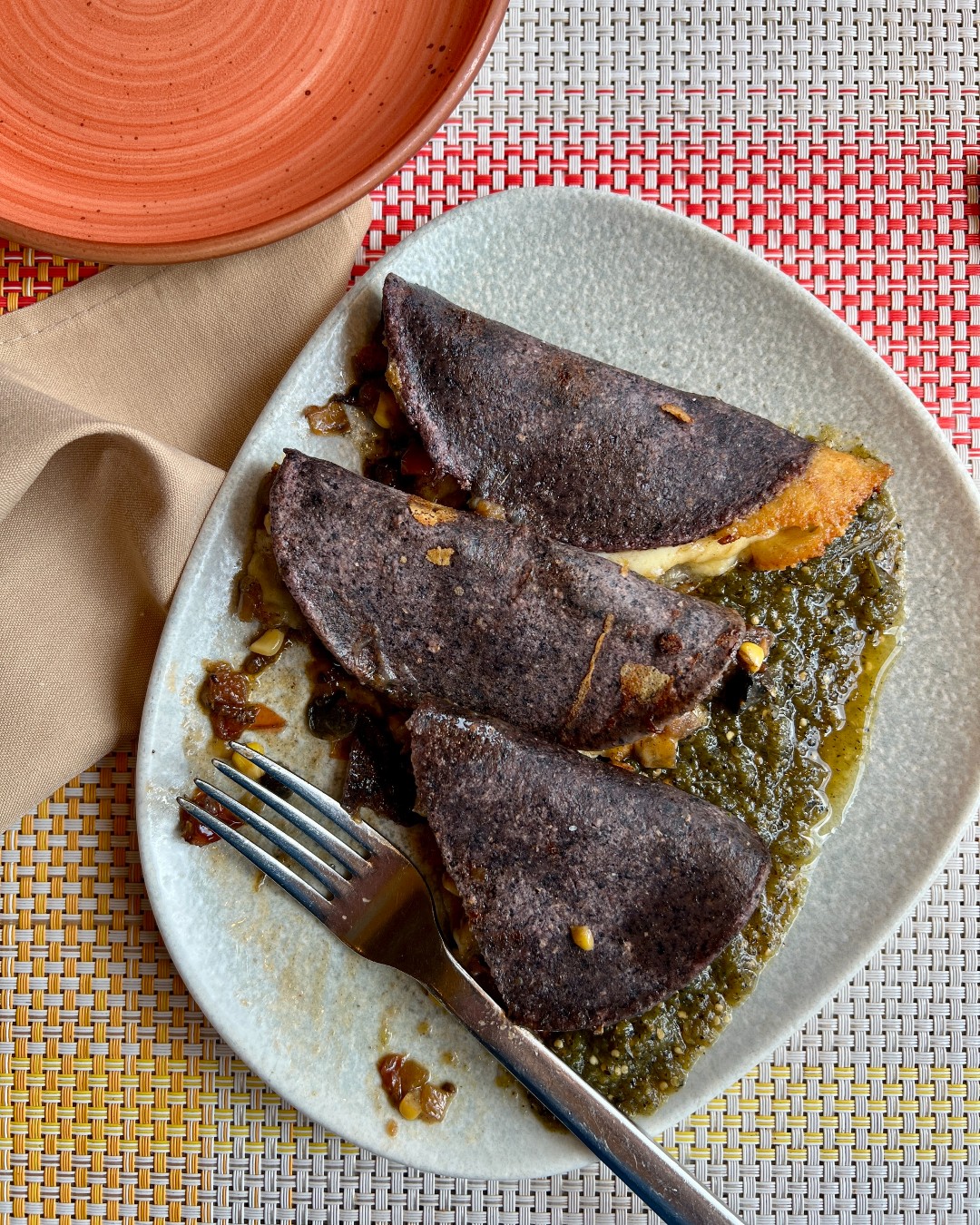 Three blue corn quesadillas with melted cheese on green salsa, served on a plate with a fork—a must-try for anyone exploring top foodie destinations.