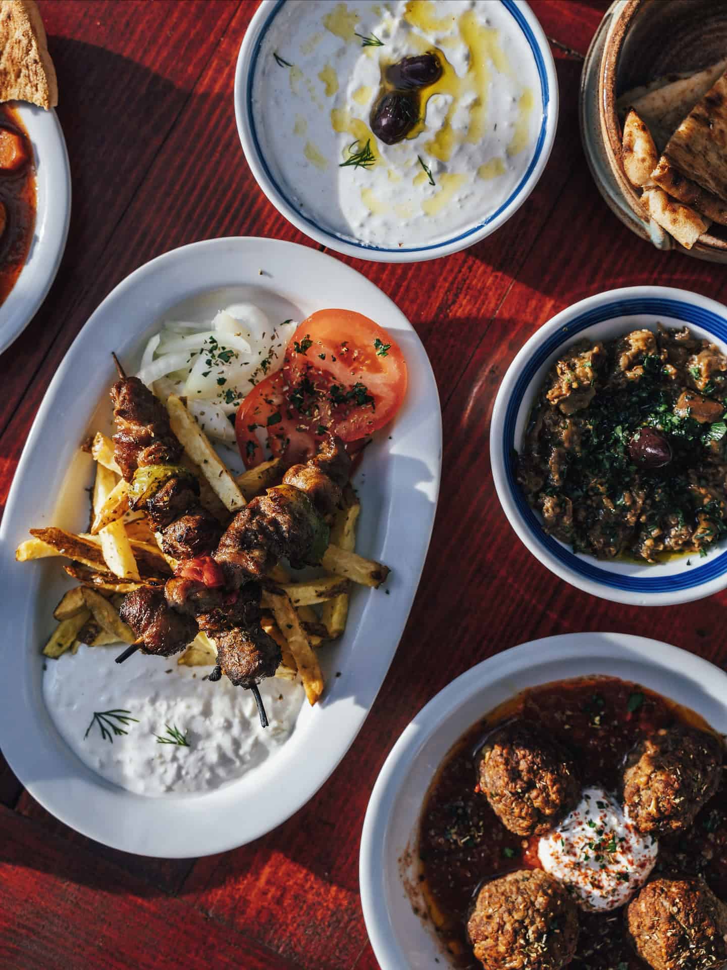 A spread of Greek dishes on a table—kebabs, meatballs, tzatziki, spinach stew, and pita bread—perfect for those exploring top foodie destinations.