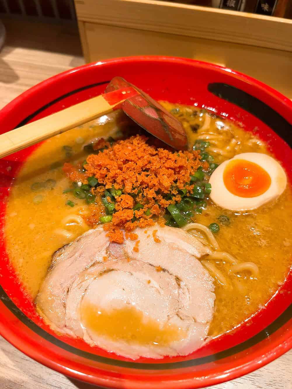 A bowl of ramen with sliced pork, half a soft-boiled egg, green onions, spicy crumbs, and broth—perfect for those exploring top foodie destinations.