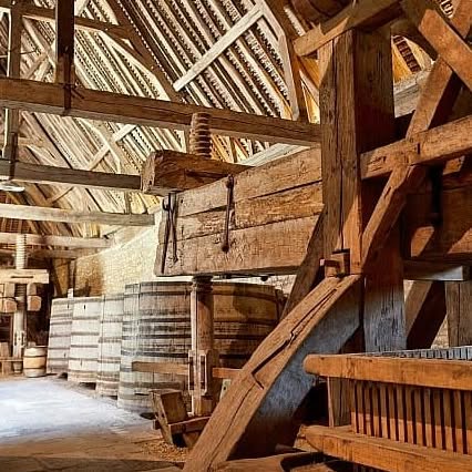 Old wooden wine press and barrels inside a rustic barn with exposed beams and warm lighting evoke the timeless charm of the French countryside—an atmosphere often savored during a luxury barge cruise.
