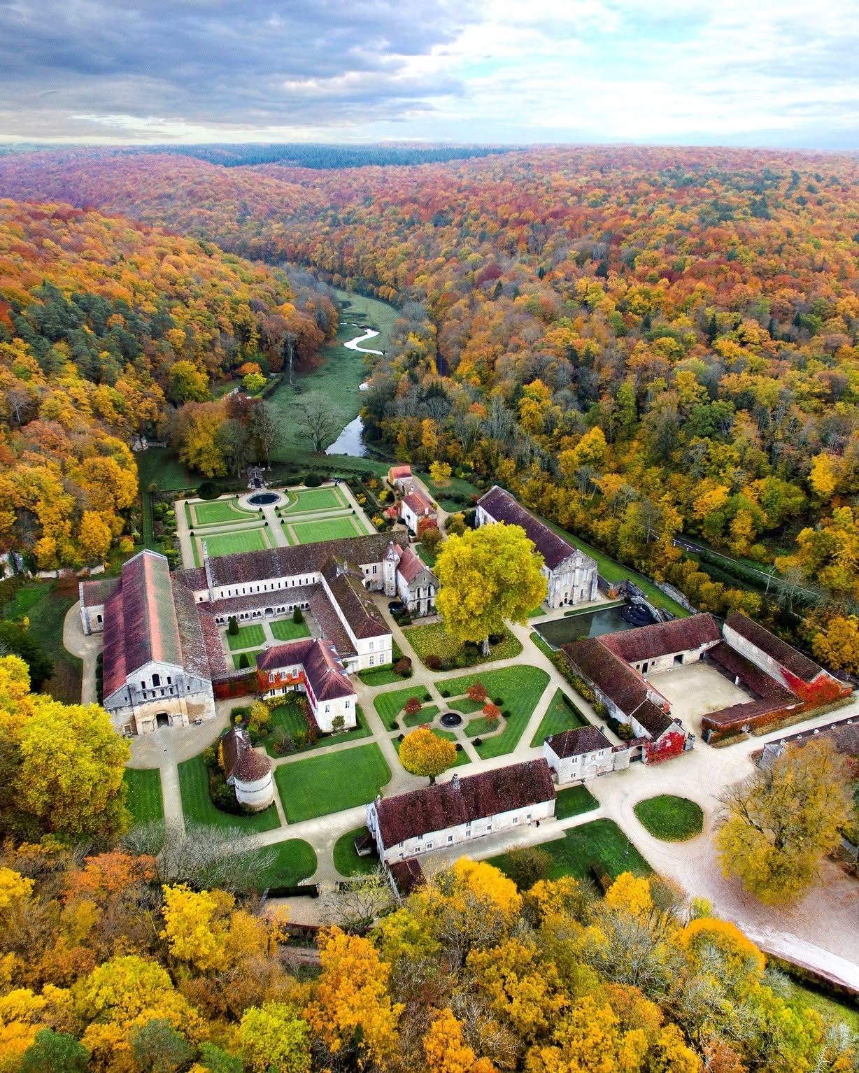 Aerial view of a large estate surrounded by colorful autumn trees and a winding river, evoking the elegance of a luxury barge cruise gliding through breathtaking countryside scenery.