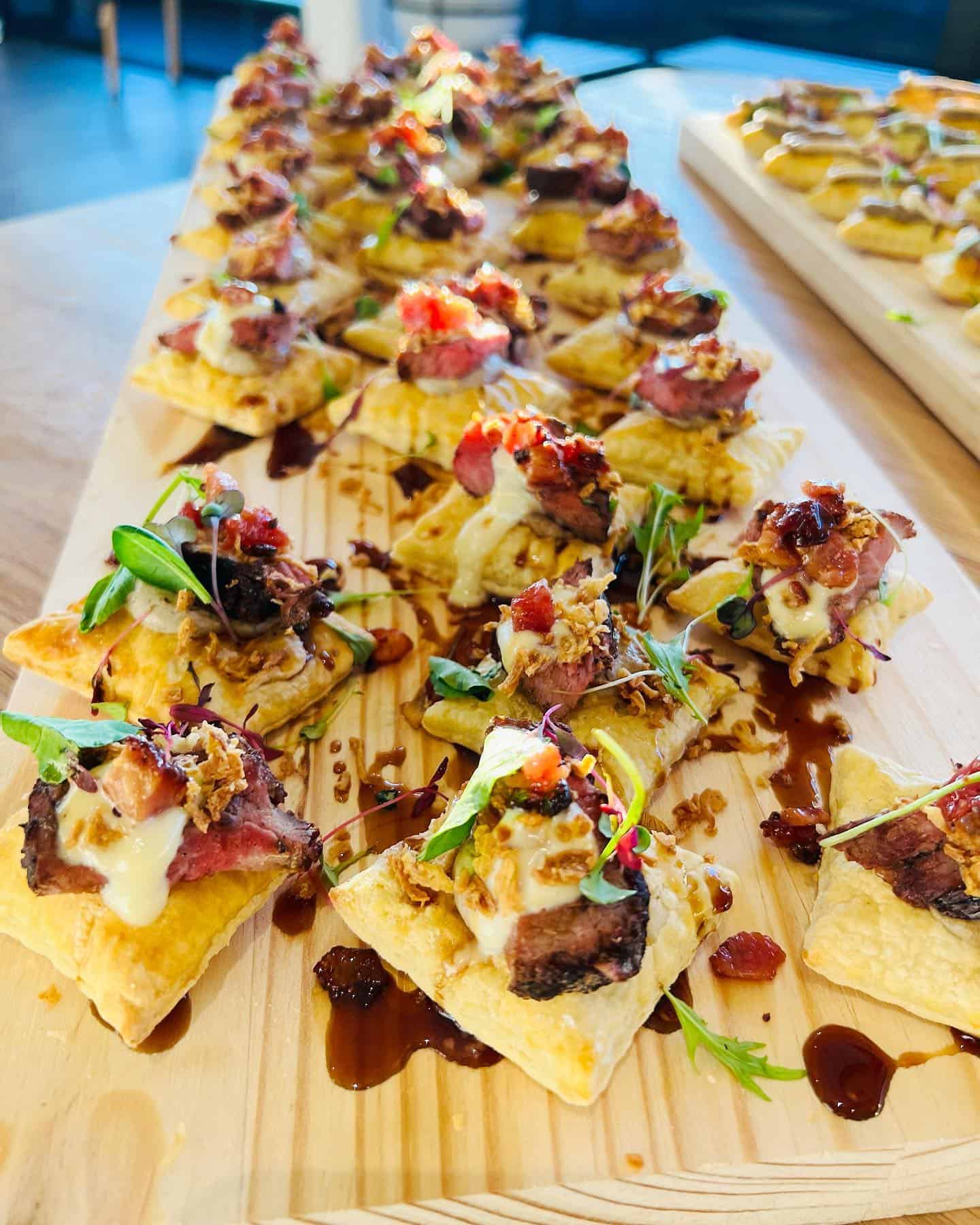 Pastry bites topped with steak, sauce, herbs, and garnishes, these treats are perfect for those exploring top foodie destinations—beautifully arranged on a wooden serving board.
