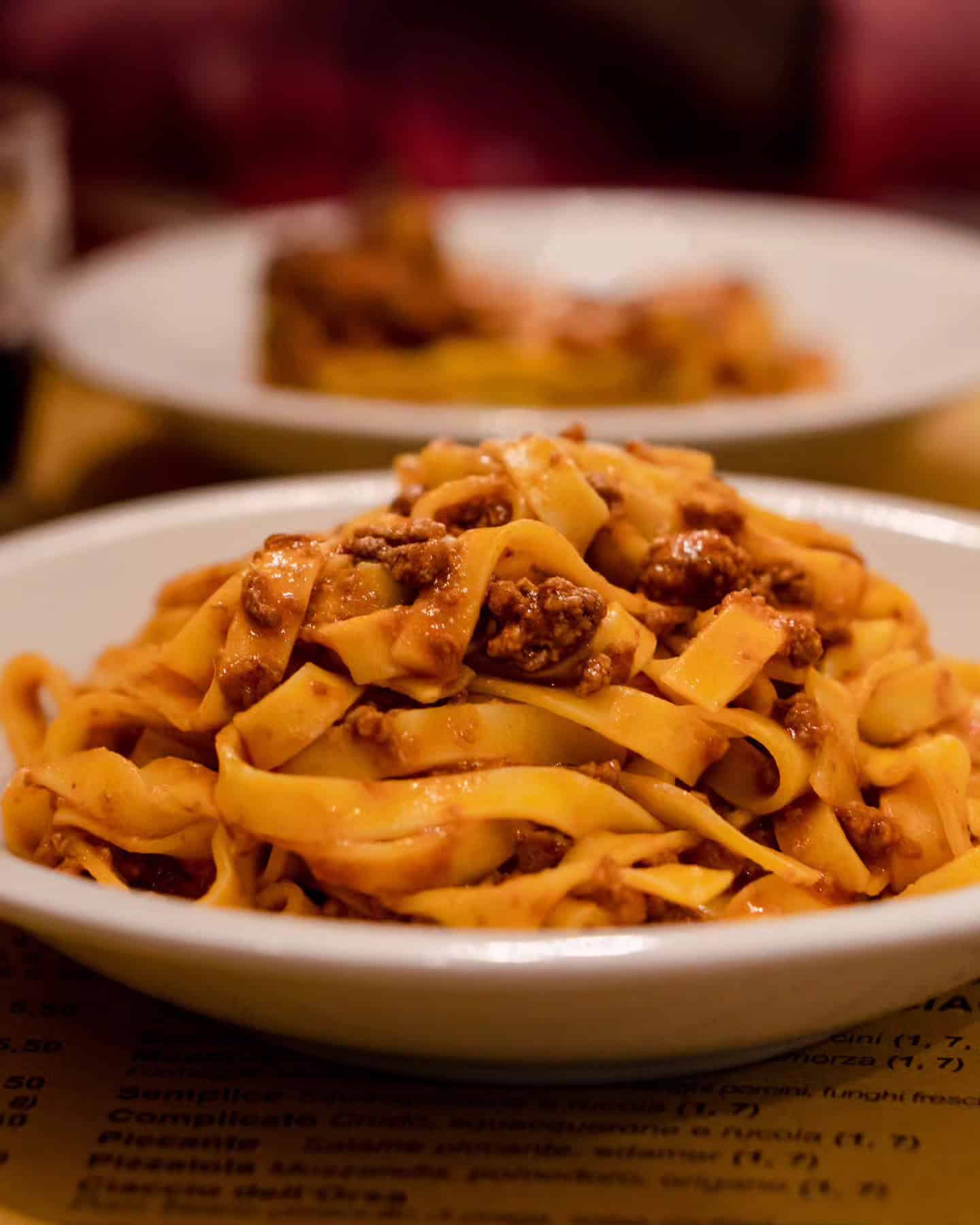 A bowl of tagliatelle pasta with rich meat sauce, served on a table in a restaurant—perfect for exploring top foodie destinations.