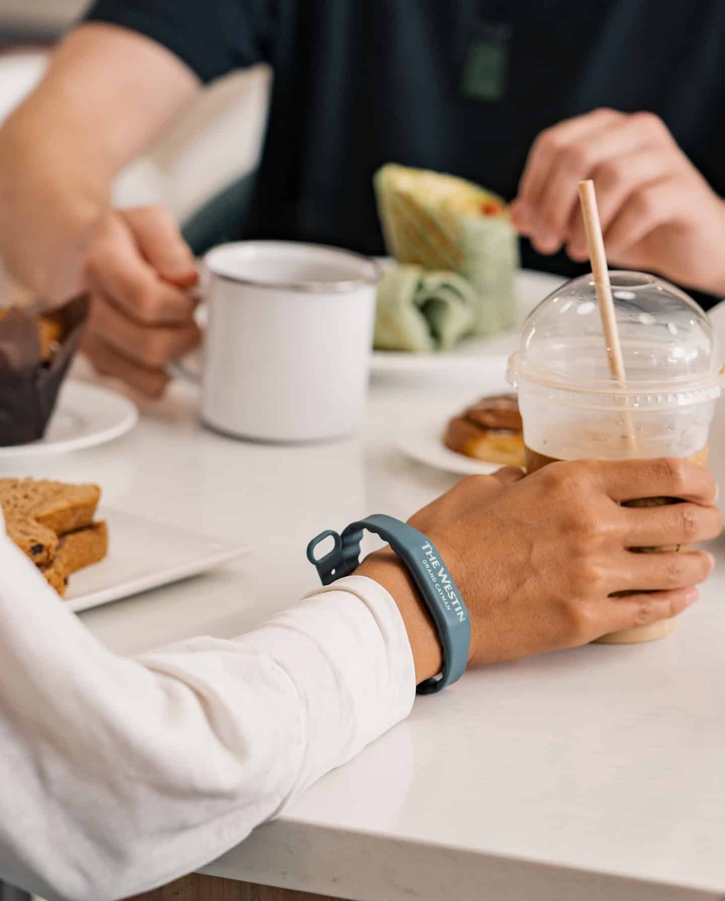 Two people dining at a table, enjoying coffee, a wrap, an iced drink, a pastry, and wearing a fitness wristband&mdash;an inviting scene that embodies the relaxed elegance of Grand Cayman luxury travel.
