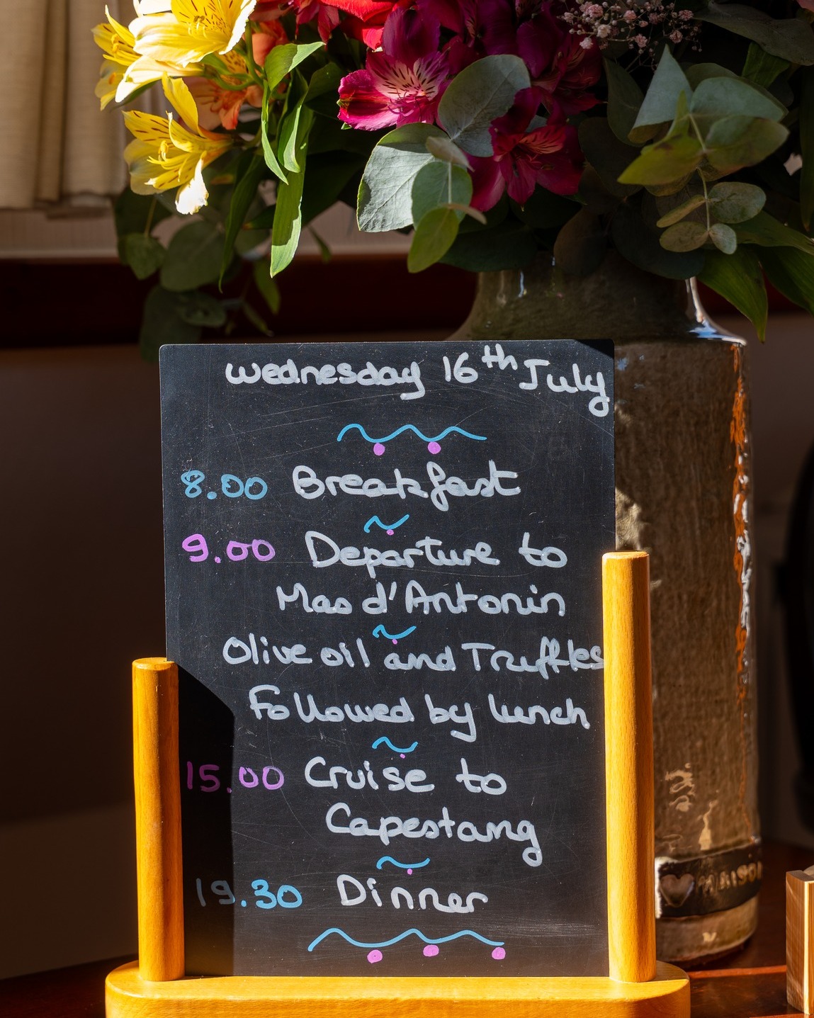 A chalkboard with a day's itinerary, flowers in the background, and sunlight shining on the board sets the scene for a luxury barge cruise.