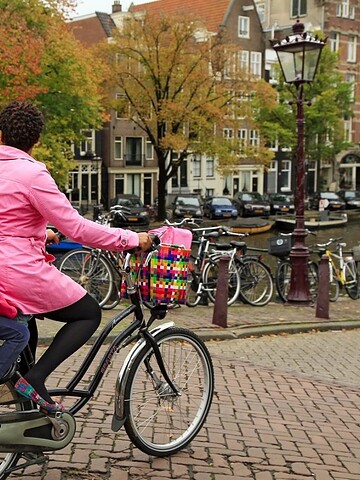Woman and child in pink jackets ride a bike by a canal with parked bikes and trees in autumn.