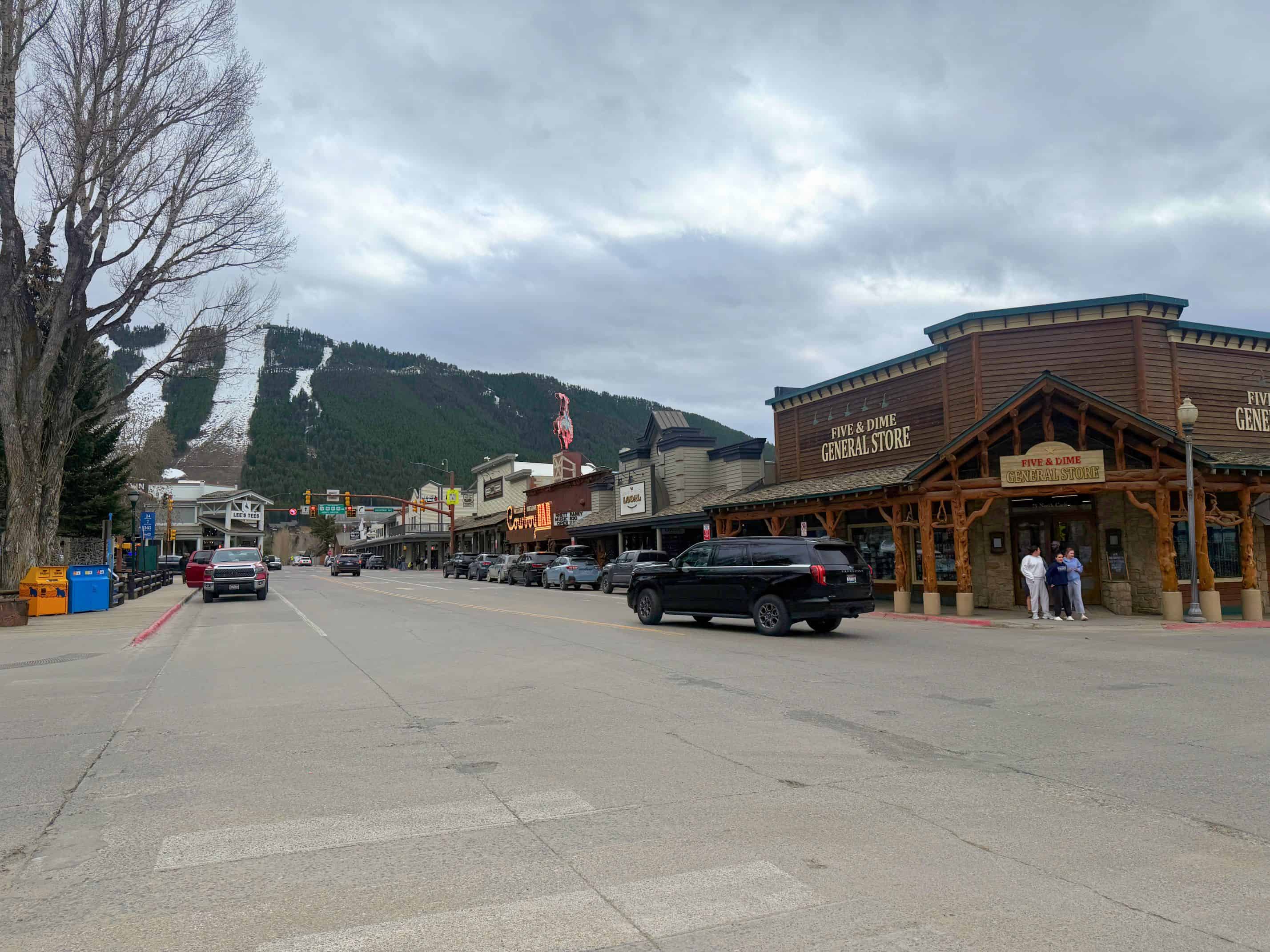 A small western-style town with shops, parked cars, a cloudy sky, and mountains in the background&mdash;just the kind of scene you&rsquo;d discover in any good Jackson Hole travel guide.