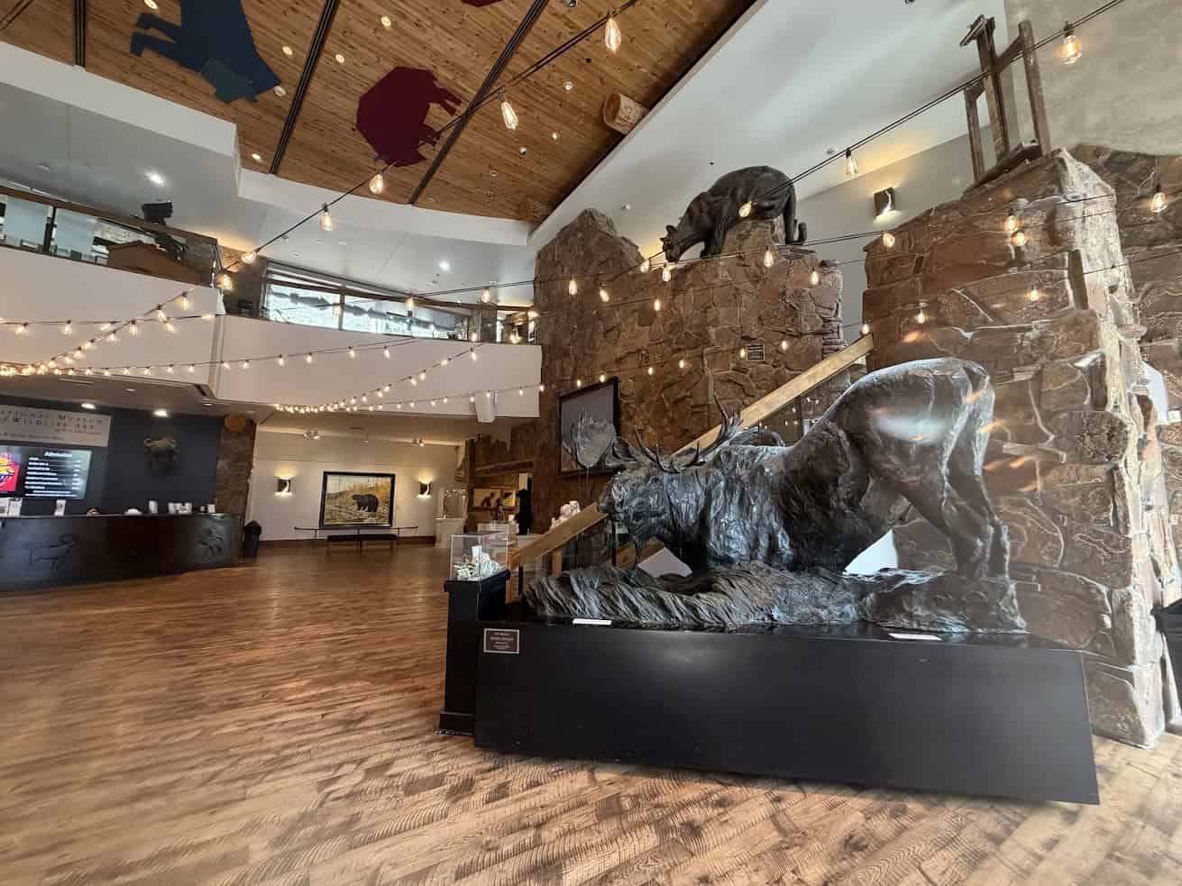 Lobby with a large moose sculpture, stone walls, animal art, string lights, and wood flooring&mdash;an inviting space that feels straight out of a Jackson Hole travel guide.